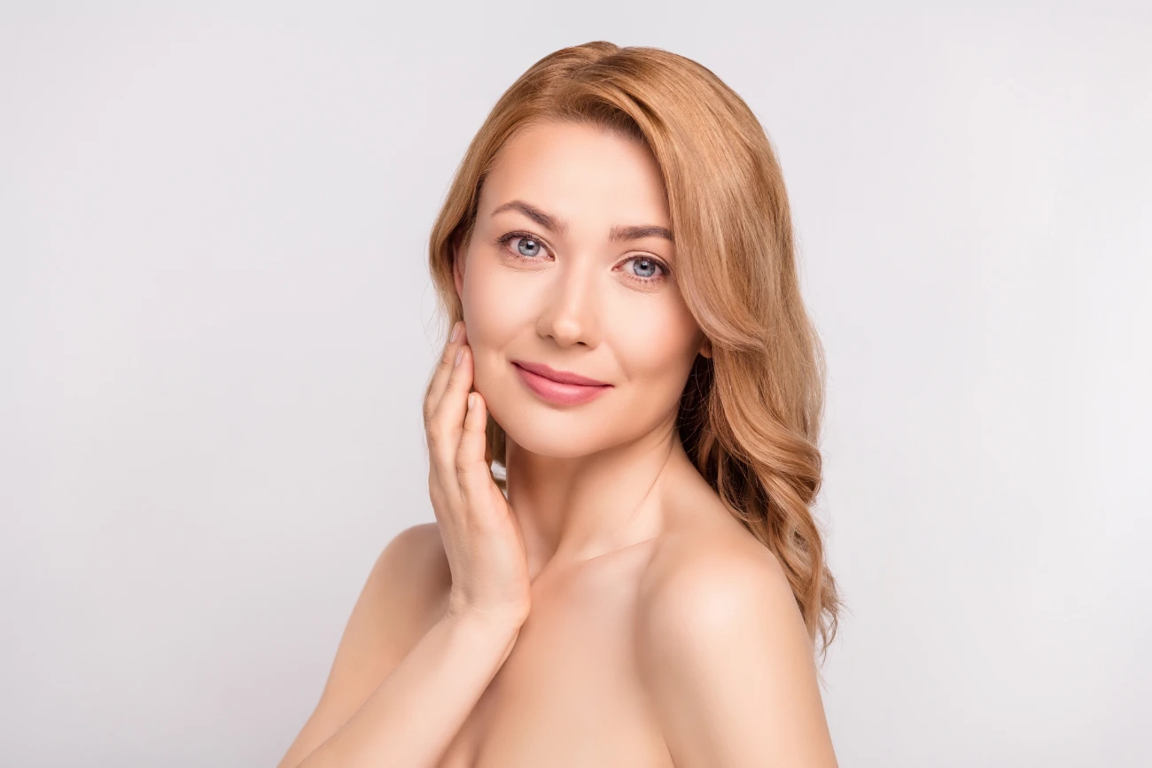 Photo portrait woman after shower smiling with nude shoulders applying cream on cheeks isolated white color background. restylane featured image