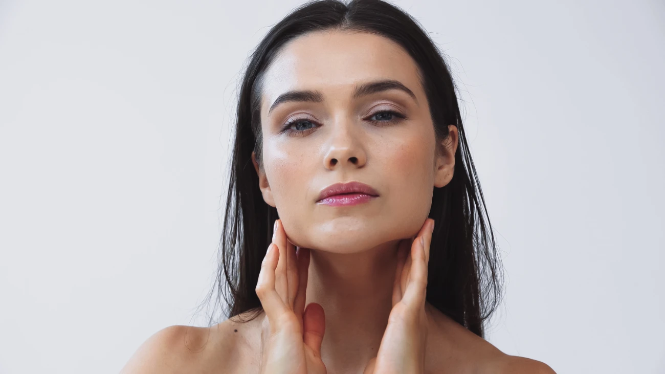 brunette woman touching perfect skin while looking at camera isolated on grey