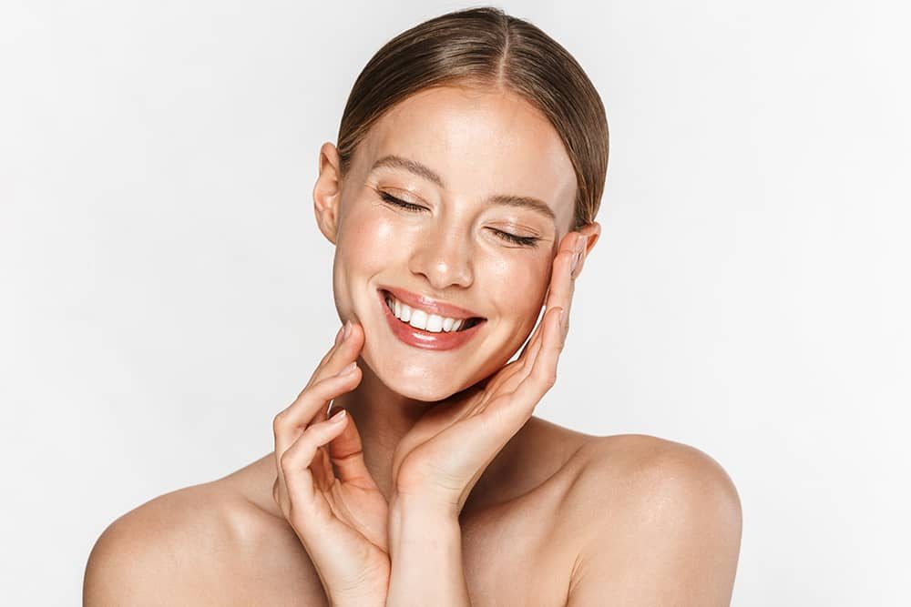 A woman with her eyes closed smiles with her hands on her cheeks.