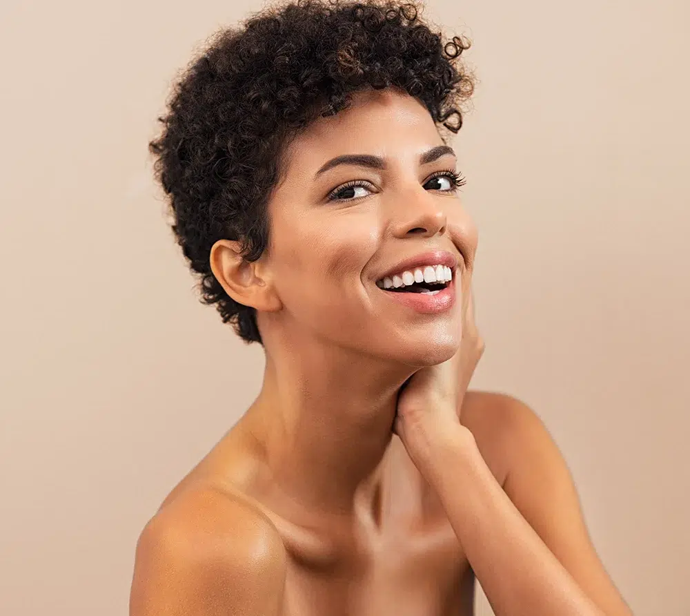 Smiling woman with short curly hair and glowing skin, highlighting natural beauty and white teeth.